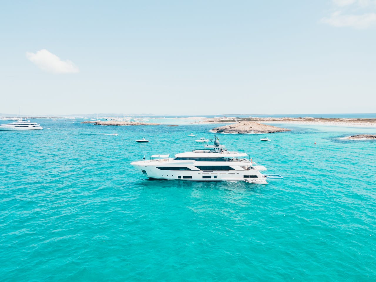 Offerings A luxury yacht sails through the vibrant turquoise waters near Ibiza, Spain, under a clear sky.