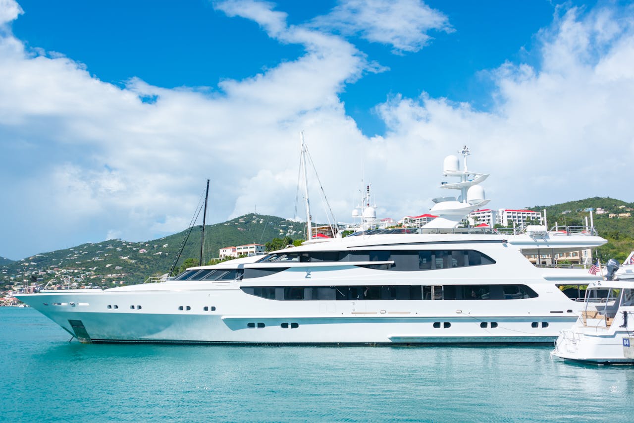 Offerings A sleek luxury yacht docked in a tropical harbor with clear blue skies and picturesque hills.