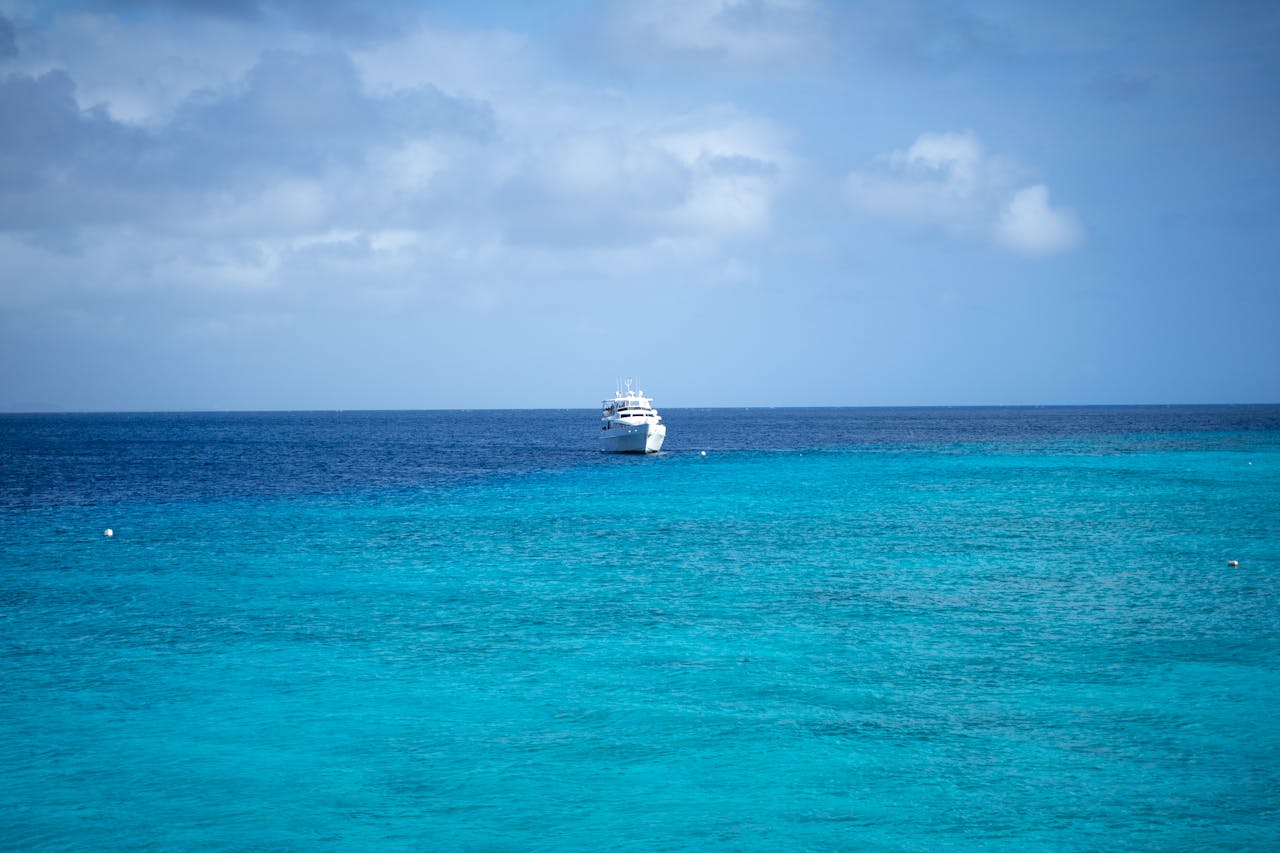 Offerings A luxury yacht sails on the vibrant turquoise waters of Curaçao under a partly cloudy sky.